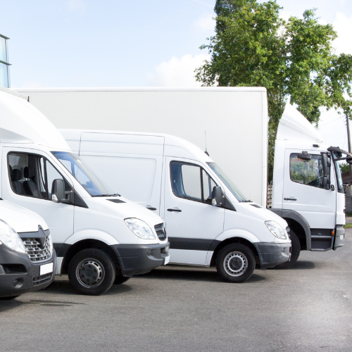 A fleet of box trucks, vans and other delivery vehicles parked in a parking lot,